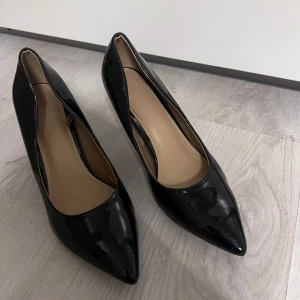 Svarta lackpumps med spetsig tå - Klassiska svarta pumps i glansigt lackmaterial med spetsig tå och smal hög klack. Klack:8cm OBS:har en liten skada längst ner klacken som inte är något man tänker på. (sista bilden)  Använd få gånger. Passar en 39/40. Då de är små i storlek 