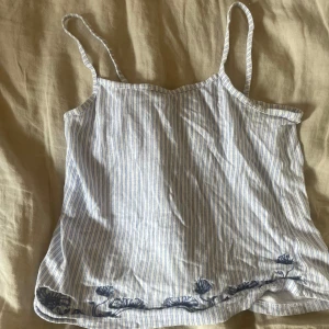 Randig linnetopp med broderi - Fråga om ni vill ha mer bilder! Söt randig linnetopp med tunna axelband i vitt och ljusblått.  Toppen är från holister.  Man kan använda som en sov linne eller bara en vanlig söt topp till vardagen.  Aldrig använd utan prislapp 