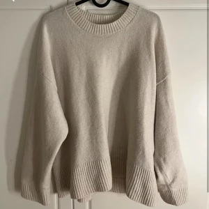 Vit stickad tröja från Stradivarius - Supermjuk och oversized vitbeige stickad tröja från Stradivarius. Tröjan har breda ribbade muddar vid ärmslut, nederkant och halsringning. Perfekt för lager-på-lager och chill dagar. Enkel att matcha med jeans eller kjol.