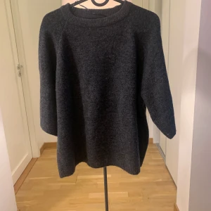 Mörkgrå stickad tröja från 157 - Mysig mörkgrå stickad tröja från 157 med rund halsringning och avslappnad passform. Perfekt för lager-på-lager och passar till både jeans och kjol. Tröjan har trekvartsärm och är superenkel att styla för en chill look.