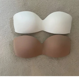 2-pack bh vit & beige - Säljer ett 2-pack vadderade bandeau toppar i mikrofiber, en i vit och en i beige. Båda är axelbandslösa och har hakknäppning bak för perfekt passform. Perfekta under toppar eller klänningar där du vill ha en clean look utan axelband.