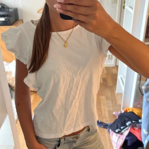 Vit blus med volangärmar - Säljer en söt vit blus med volangärmar och spetsdetaljer längs ärmsluten. Blusen är i luftig bomull och har en rak, lite croppad passform. Perfekt till jeans eller kjol för en fräsch och enkel look.
