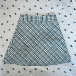 Rutig kortkjol från Sugar Thrillz XS - Supersöt slutsåld rutig kortkjol från Sugar Thrillz i blå och vita toner. Kjolen har A-linjeform och är fodrad med ljusblått tyg på insidan. Perfekt för dig som gillar preppy vibes och vill sticka ut med en klassisk look.