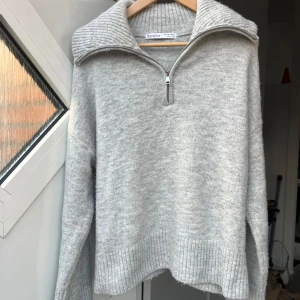 Ljusgrå stickad half zip-tröja Bershka - Mysig ljusgrå stickad tröja från Bershka med ribbad krage och half zip-dragkedja. Tröjan har lång ärm, bred ribbad mudd vid ärmslut och nederkant samt en loose passform. Perfekt för lager-på-lager och chill dagar. Vill få den såld snabbt så därav priset. Har inte sett några fläckar eller defekter! Sparsamt använd! Kan såklart disskutera priset🥰🥰