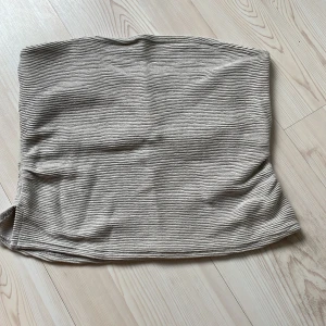 Beige ribbad tubtopp från H&M - Säljer en beige ribbad tubtopp från Divided. Toppen är axelbandslös och har en snygg struktur med horisontella ränder i tyget. Perfekt att styla med jeans eller kjol för en clean look. Mjuk och stretchig för skön passform.