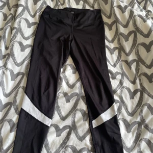Svarta leggings från H&M Sport - Svarta leggings från H&M Sport med vita detaljer vid benen. Sitter tight och är perfekta för träning eller chill. Gjorda i stretchigt syntetmaterial som andas och ger bra rörelsefrihet.