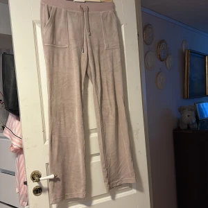 Beige mjukisbyxor från Juicy Couture - Supermjuka beige mjukisbyxor från Juicy Couture med bred resår och snörning i midjan. Byxorna har raka ben, stora fickor fram och bak med snygga JC-detaljer i silver. Perfekta för chill dagar eller när du vill vara extra comfy.
