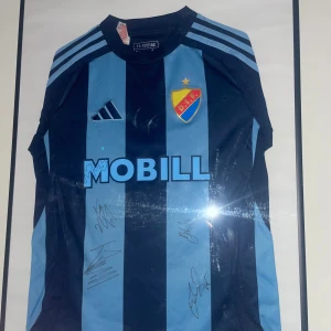 Djurgården fotbollströja  -  en Djurgården fotbollströja från Adidas med breda marinblå och ljusblå ränder, klubbmärke på bröstet och sponsortryck. Tröjan har korta ärmar och klassiska Adidas-ränder på axlarna. Perfekt för dig som älskar DIF! signerad av Tobias Gulliksen, keita Kosugi, Albin Ekdal, och Jakob rinne  (säljer ej ska se vad jag kan få den för ni får buda) start 4000kr 