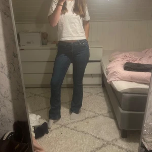 Low waist bootcut jeans tall från Gina Tricot  - Säljer ett par blå bootcut jeans från Gina Tricot i storlek 38. Jeansen har klassisk femficksdesign, låg midja och snyggt utsvängda ben. Dessa är i tall modellen och är långa på mig som är 177. Dom är använda men i bra skick, nypris är 499