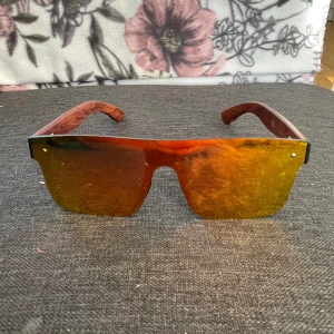 Dubery solglasögon med spegelglas - Säljer ett par feta solglasögon från Dubery med stora, rektangulära spegelglas i orange och gult. Skalmarna har trälook och loggan är ingraverad på sidan. Perfekt accessoar för dig som vill sticka ut med en modern vibe.