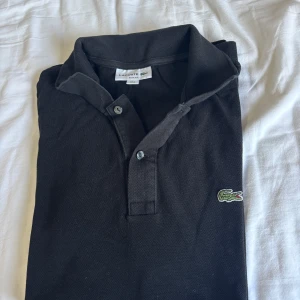 Svart pikétröja från Lacoste - Hej! Säljer denna piké för att den är för slim på min kropp, fick den av min morbror för att han tömde sin garderob och väljer att sälja vidare, storlek m slim fit och den är i bra kvalitet fortfarande 😍
