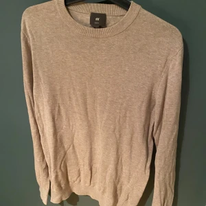 Beige slim fit tröja från H&M - En stilren beige tröja från H&M i slim fit-modell. Tröjan har rund halsringning, långa ärmar och är tillverkad i mjuk bomullsmix. Perfekt för dig som gillar en enkel och clean look med en neutral färg som passar till allt.