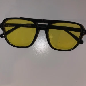 Tomford liknade glasögon  - Coola pilotinspirerade glasögon med svart ram och gula glas. Perfekt accessoar för dig som vill sticka ut och ge din stil en retrovibe. Bågarna är i plast och har en klassisk form som passar de flesta ansikten.