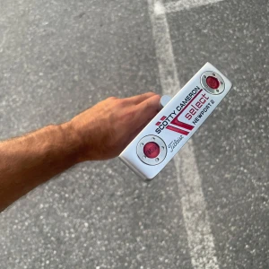 Scotty Cameron Select Newport 2 - En stilren och ikonisk putter med modern design och röda detaljer. Perfekt för dig som vill ta ditt golfspel till nästa nivå och sticka ut på greenen. Passar både nybörjare och erfarna golfare som vill ha kvalitet och känsla i varje slag.
