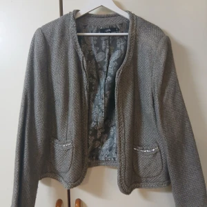 Grå cardigan jacka från Isolde - Snygg grå cardigan jacka från Isolde med vävd struktur och dekorativa fickor framtill. Jackan har ett elegant mönstrat innerfoder och rundad halsringning. 