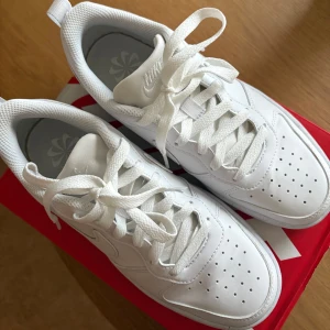 Vita Nike sneakers med snörning - Fräscha helvita Nike sneakers med klassisk design och låg profil. Skorna har ventilerande perforeringar på tån, tydlig swoosh-logga på sidan och bekväm vadderad insida. Ovandel i syntet och skinn, platt sula och snörning för perfekt passform. Har använt dom en gång utöver det är dom som nya, kan tvätta undersidan om det skulle viljas.🥰nypris:670kr