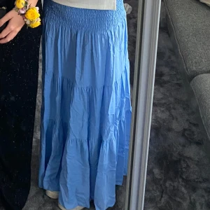 Blå långkjol från Ezence - Supersöt blå långkjol från Ezence med smockad midja och volangiga lager. Kjolen är luftig. Fin att matcha med crop tops eller stickade tröjor. 