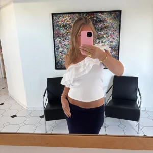 Vit off-shoulder topp med volang - Supersöt vit off shoulder topp med stor volangdetalj över axeln. Ribbat material på toppen och ett linne aktigt material på volangerna. Perfekt till jeans eller kjol❣️