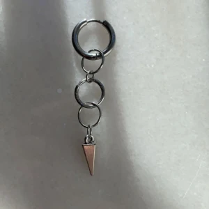 Silvrigt örhänge med kedjor och kon - Coolt silvrigt örhänge med flera ringar i kedja och en spetsig konformad detalj längst ner. Ger en edgy vibe och passar perfekt för dig som gillar unika accessoarer.