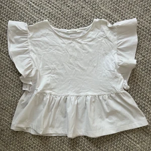 Vit volangblus från Reserved XS - Supersöt vit blus från Reserved i storlek XS. Toppen har breda volangärmar och volang nertill som ger en luftig och trendig look. Tillverkad i mjuk bomull med rund halsringning. Perfekt för dig som gillar romantiska detaljer och en feminin stil.