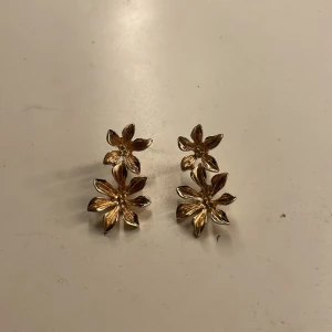 Guldiga blomörhängen - Snygga örhängen i guldton med dubbla blommor på varje örhänge. De har en cool, tredimensionell design där varje blomma har sex blad och en glansig finish. Perfekta för att ge din look en extra touch av stil. Tvättar självklart av dem innan jag skickar dem 💓