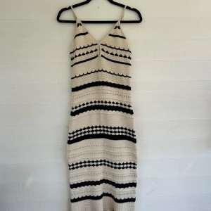 Stickad långklänning - Supersnygg stickad långklänning från H&M i beige och svart med smala axelband och v-ringning. Klänningen har ett coolt randigt mönster och är figurnära med en bohemisk vibe. Perfekt för sommardagar eller festivalhäng! Aldrig använd då den tyvärr inte passar mig!