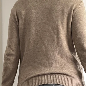 Beige stickad tröja med rund hals - En enkel och stilren beige stickad tröja med rund halsringning och ribbade muddar vid ärmslut och nederkant. Tröjan har en normal passform och är perfekt för lager-på-lager under kyliga dagar. Mjuk och skön känsla mot huden. Ett litet hål på bröstet, syns knappt.