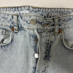 Ljusblå wide jeans med slitningar - Säljer ett par ljusblå jeans med wide fit och hög midja. Jeansen har slitna detaljer och hål vid knäna för en cool, avslappnad look. Klassisk femficksmodell med knappar i gylfen. Perfekta för dig som gillar en trendig och bekväm stil.