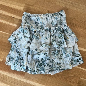 Blommig volangkjol från KappAhl XS - Supersöt kort volangkjol från KappAhl i blommigt mönster med gröna och gula toner på ljus botten. Kjolen har smock i midjan och flera lager volanger som ger en flowy känsla. Perfekt för vår och sommar! Använd varsamt så inte ny skick, men inget man märker när man har på sig den! Skriv vid minsta lilla. 🥰