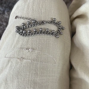 Två silverfärgade armband - Säljer två snygga armband! Ett chunky kedjearmband med kulor och ett tunt, minimalistiskt armband med små detaljer. Båda är i silverfärg och passar perfekt för att mixa och matcha till olika outfits. Aldrig använd