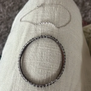 Silverfärgat armband och halsband - Säljer ett stilrent armband i silverfärg med fyrkantiga länkar och ett tunt halsband med små klara stenar på rad. Båda smyckena har en modern och minimalistisk vibe, perfekta för att lyfta din outfit med lite extra bling. Aldrig använd 