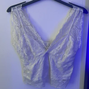 Vit spetsig linnetopp från Amisu - Supersöt vit linnetopp från Amisu i genombruten spets med blommigt mönster. Djup v-ringning både fram och bak, ärmlös och croppad passform. Perfekt att styla med jeans eller kjol för en trendig look.