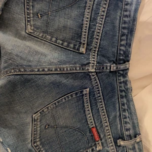 Guess jeansshorts låg midja blå - Säljer ett par snygga blå jeansshorts från Guess med låg midja och slitna detaljer. Klassisk femficksmodell i 100% bomull med råa kanter och cool tvätt. Perfekta för dig som gillar en avslappnad och trendig stil.