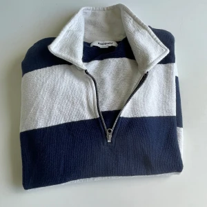 Randig half zip tröja från Kappahl - Snygg och stilren tröja med breda marinblå och vita ränder. Har en halv dragkedja framtill och en högre krage som ger ett sportigt och klassiskt utseende. Perfekt för vardagsbruk eller en avslappnad outfit.  🔹 Storlek: Medium 🔹 Färg: Marinblå/vit 🔹 Skick: Bra begagnat skick – inga fläckar eller hål