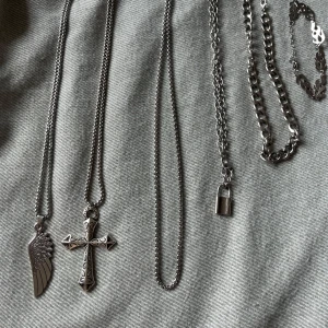 Paket med silvriga kedjesmycken - Flera silvriga halsband och ett armband i metall. Halsbanden har olika hängen: ett med vinge, ett med kors och ett med hänglås. Kedjorna varierar i tjocklek och stil. Armbandet har coola flammor som länkar. Perfekt för dig som gillar edgy accessoarer. Säljes för 10kr styck eller 30kr för hela paketet. Använda typ en gång.