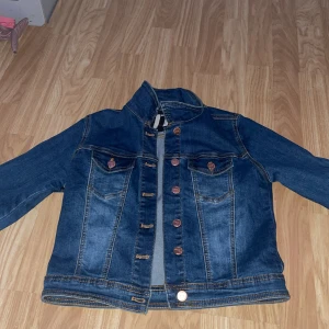 Mörkblå jeansjacka från 77th, strl 34 - Snygg mörkblå jeansjacka från 77th med klassiska kopparfärgade knappar och två bröstfickor. 