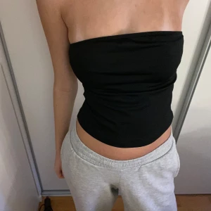 Svart bandeau tubtopp - Enkel och stilren svart bandeau tubtopp som sitter tight och ärmlös. Perfekt att matcha med jeans eller kjol för en clean look. Mjuk och stretchig, passar dig som gillar minimalistiska plagg.