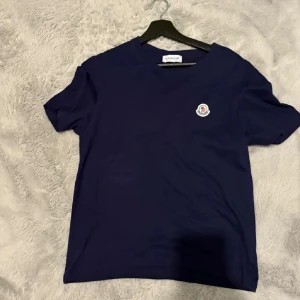 Mörkblå Moncler t-shirt i bomull - Snygg mörkblå t-shirt från Moncler med klassisk passform och rund hals. T-shirten har korta ärmar och en liten broderad Moncler-logga på bröstet. (Säljer av kläder så kolla gärna min sida och se om du är intresserad av något annat)