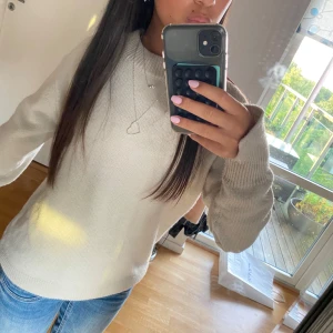 Beige stickad tröja från H&M - En stilren beige stickad tröja från H&M i storlek S. Tröjan har en klassisk rund halsringning, ribbade muddar och lång ärm. Perfekt för lager-på-lager och enkel att matcha med jeans eller kjol.