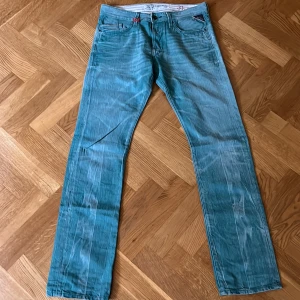 Turkosa Replay jeans straight fit - Snygga turkosa jeans från Replay med raka ben och klassisk femficksdesign. Jeansen har coola slitningar och detaljer vid fickorna samt Replay-logga. Perfekta för dig som vill sticka ut med färg och stil. Materialet är klassisk denim.
