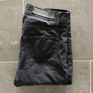 Tiger Of Sweden Jeans - Svarta slim jeans från Tiger Of Sweden i storlek 30/32. Klassisk femficksmodell med svarta sömmar och läderpatch bak i midjan. Snygg passform med smala ben och normal midja. Perfekta till sneakers eller boots.
