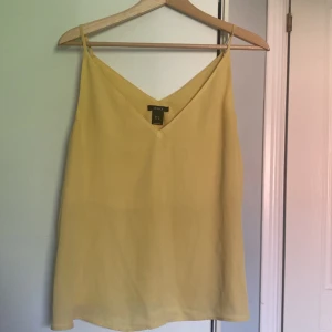 Gul linnetopp från Lindex - Snygg gul linnetopp från Lindex i storlek M. Knappt använt. Toppen har smala axelband och v-ringning både fram och bak. Perfekt för varma dagar och enkel att styla med jeans eller kjol. Luftigt material som känns lätt mot huden.