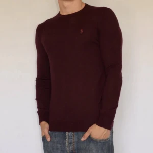 100% merinoull tröja Ralph lauren - Vinröd långärmad tröja från Polo Ralph Lauren i slim fit-modell. Tillverkad i mjuk och tvättbar merinoull, med klassisk rund hals och diskret broderad logga på bröstet. Perfekt för dig som gillar stilrena och bekväma plagg.