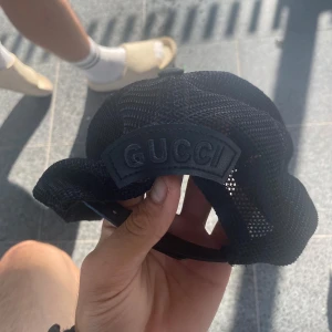 Svart keps från Gucci med tryck  - Snygg svart keps från Gucci med mesh på sidorna och justerbar baksida. Skärmen har diskret GG-mönster och ovansidan är dekorerad med färgglada djurmotiv. Kepsen är i bomull och har tydlig Gucci-logga både invändigt och bak.