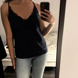 Mörkblått linne från Shein - Snyggt mörkblått linne från Shein med spetsdetaljer vid axelbanden. Perfekt för en stilren look. Linnet har en enkel design med smala axelband och en mjuk, flytande passform.