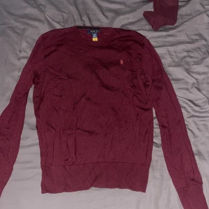 Vinröd tröja från Polo Ralph Lauren - Snygg vinröd tröja från Polo Ralph Lauren med klassisk rund hals och diskret broderad logga på bröstet. Tröjan är långärmad och har ribbade muddar vid ärmslut och nederkant. Perfekt för dig som gillar stilren och enkel design.