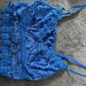 Blå spetsig linnetopp från SHEIN - Supersöt blå linnetopp från SHEIN med tunna justerbara axelband och detaljerad spets med blommönster. Toppen är ärmlös och har en feminin, croppad passform som ger en trendig vibe. Perfekt att styla med jeans eller kjol för en cool look.