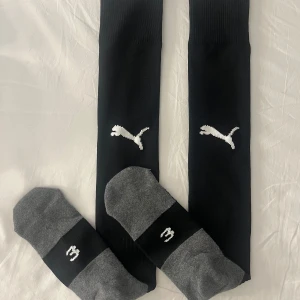 Oanvända svarta fotbollsstrumpor från Puma - Ett par svarta fotbollsstrumpor från Puma. Helt oanvänd då de inte kommit till användning någon gång. De är mycket stretchiga och är ribbade upptill. Ungefär storlek 38-41