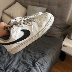 Nike Dunk Low vit/svart, stl 38 - Snygga Nike Dunk Low sneakers i vitt skinn med svart swoosh och klassisk siluett. Skorna har perforerad tå, platt sula och snörning. Perfekta för dig som gillar streetstyle och vill ha en ikonisk sneaker i garderoben.