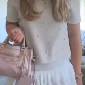 Beige topp med pärldetaljer - Superfin beige topp med kort ärm och ribbad rund halsringning. Toppen är dekorerad med små pärlor framtill som ger en söt och trendig look. Perfekt att styla med både jeans och kjol! Storlek m men skulle säga att den är liten i storleken! Den skulle även passa från xs-S! Använd två gånger ingen tecken på användning 